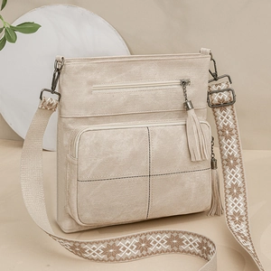 Detail of beige crossbody bag with double zippers, tassel charm and ethnic strap