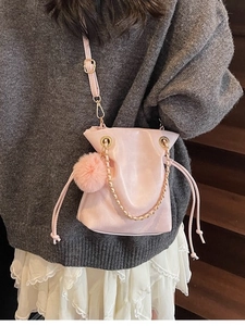 Sac seau rose avec cordon de serrage, chaîne dorée et pompon porté par un modèle