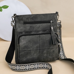 Close-up of dark grey bag with double zippers, tassels, and a geometric patterned strap