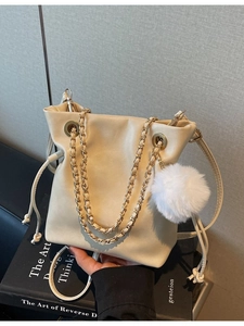 Sac seau à cordon crème avec pompon en peluche et bandoulière en chaîne sur fond minimaliste