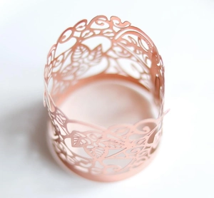 Macro detail of laser-cut pink paper wrap with floral bird patterns for LED candles