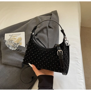 Close-up of black dumpling bag with pearl embellishments on a suede texture fabric
