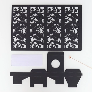 Detailed laser-cut black paper candle shade with intricate scroll patterns and base