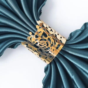 Detail of gold hollow rose napkin ring on dark green satin fabric with mirror finish