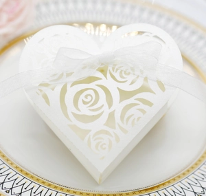 Close-up of white heart-shaped wedding favor box with laser-cut rose patterns and ribbon