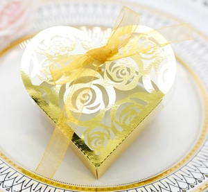 Macro view of gold heart wedding favor box with hollow rose patterns and organza ribbon