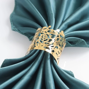 Macro view of gold plated hollow rose napkin ring on a dark green satin fabric