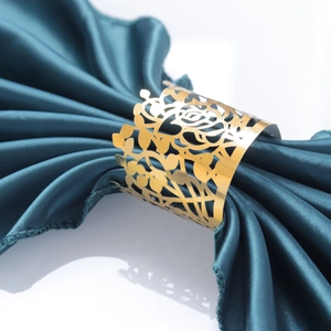 Close-up of a hollow rose gold metal napkin ring featuring intricate floral cutout details