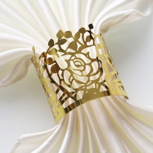 Detailed close-up of hollow gold rose napkin ring on a white satin cloth background