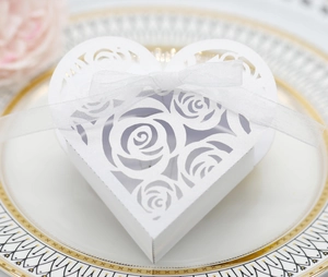 Detailed laser-cut heart favor box with rose patterns and white ribbon on a plate