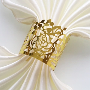 Detail showing laser-cut golden rose napkin ring on white satin fabric for weddings