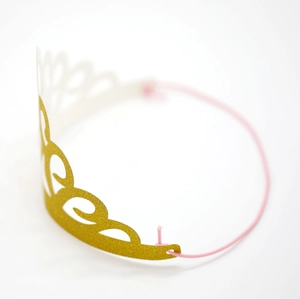 Detail view of a glittery golden party crown with pink elastic band on white background