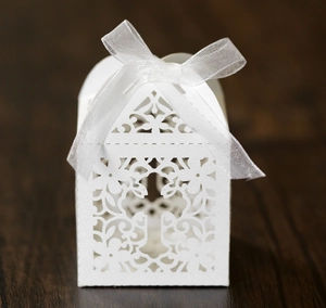 Detail of white laser-cut wedding favor box featuring a cross design and organza bow