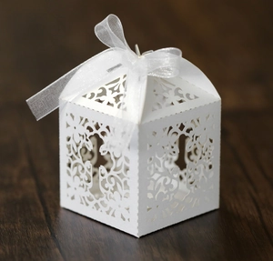 Close-up of white laser-cut wedding favor box with floral patterns and organza ribbon