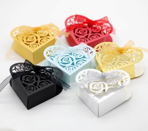 Detailed view of heart-shaped laser cut favor boxes with rose patterns and satin ribbons