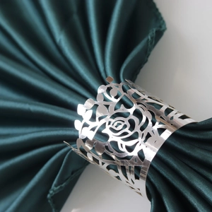 Elegant silver metal napkin ring with hollow rose pattern on dark green silk fabric