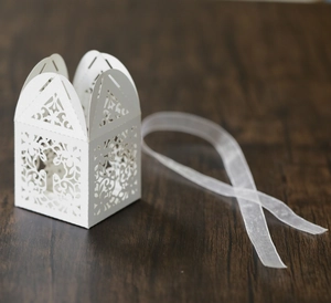 Detail of laser-cut cross floral wedding favor box with a white ribbon on wood