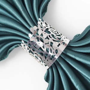 Detail of silver metal napkin ring with hollow rose pattern on green satin cloth