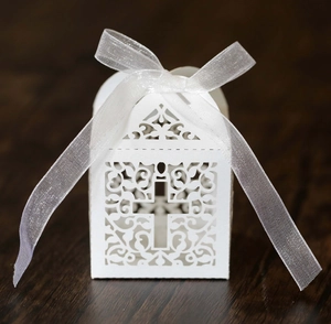 Detail of white laser-cut wedding favor box with cross pattern and organza ribbon bow
