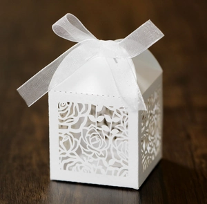 Detailed laser-cut white wedding favor box with rose patterns and a satin ribbon bow