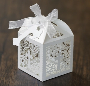 Close-up of white laser-cut wedding favor box with cross pattern and white ribbon
