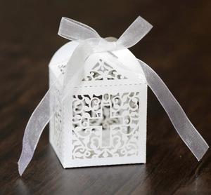 Close-up of white laser-cut wedding favor box with cross design and organza ribbon
