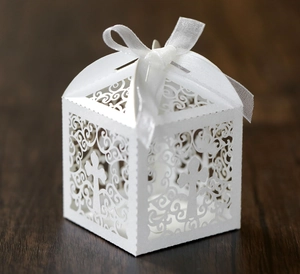 Detail of white laser-cut wedding favor box with cross pattern and white organza ribbon