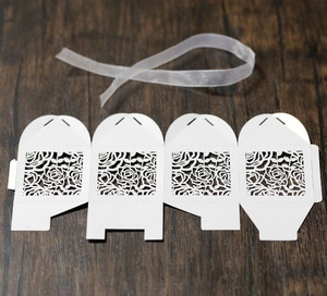Flat lay of laser-cut white wedding favor box template with rose patterns and ribbon