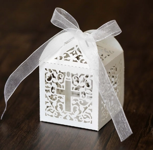 Detailed view of white laser-cut wedding favor box with cross design and organza ribbon