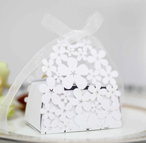 Close-up of laser-cut white paper wedding favor box with floral patterns and a ribbon bow