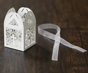 Close-up of laser-cut white cross favor box with elegant ribbons on wooden surface
