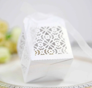 Detail of white laser-cut wedding favor box with intricate floral patterns and organza ribbon