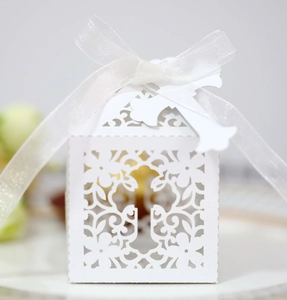Macro view of white laser-cut hollow cross favor box with decorative silk ribbon