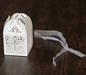 Close-up of white laser-cut cross gift box with elegant white ribbon on wood table