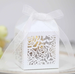 Macro shot of white hollow wedding candy box with laser-cut rose patterns and white ribbon
