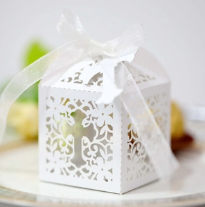 Macro shot of white laser-cut wedding favor box with cross pattern and ribbon
