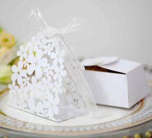 Detail of laser-cut white wedding favor boxes with floral hollow patterns and ribbons