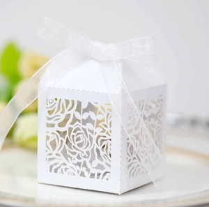 Detail of white laser-cut wedding favor box with rose patterns and organza ribbon bow