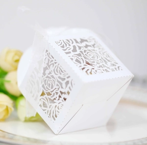 Close-up of laser-cut rose patterns on white wedding favor boxes with ribbon bow
