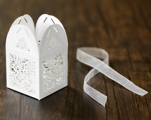 Detail of white laser-cut rose hollow favor box with chiffon ribbon on wood background