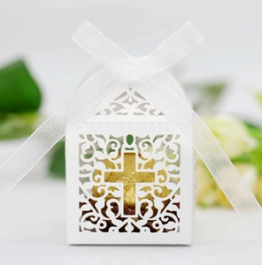 Close-up of white laser-cut favor box with hollow cross design and white ribbon bow