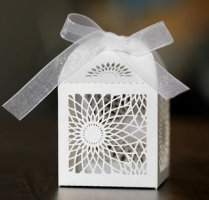 Macro detail of laser-cut house-shaped favor box with white organza ribbon bow