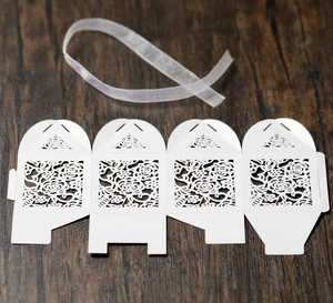 Detailed flat lay of laser-cut white rose favor box with a sheer organza ribbon on wood