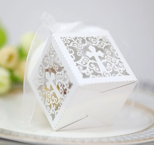 Close-up of white laser-cut wedding favor box with cross pattern and silk ribbon