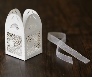 Detail of laser-cut sunflower pattern on white favor box with translucent ribbon