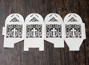 Detailed laser-cut white wedding favor box with cross pattern on dark wooden background