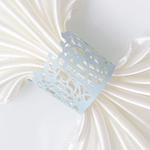 Detailed close-up of light blue laser-cut floral paper napkin ring on white satin fabric