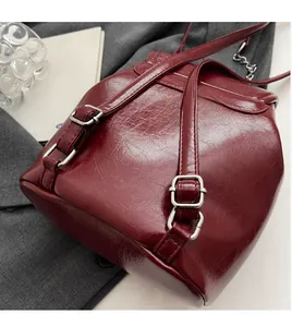Detail of burgundy glossy leather backpack featuring silver buckles and chain strap