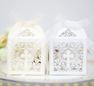 Close-up of laser-cut cross candy boxes in white and cream with elegant organza ribbons