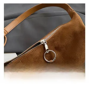 Close-up of brown suede shoulder bag with silver zipper and wooden bead charm details